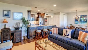 A modern living room with a sofa, a glass coffee table, and a dining area with chairs. - Sea Gull #202: Beachfront 2 Bedroom 2 Bathroom With Spectacular Views and 24 Hour Management (Port Aransas)