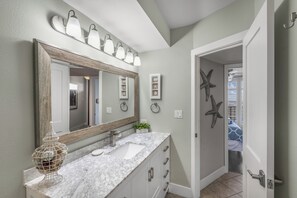 A bathroom with a large mirror, a sink, and a vanity with drawers. There are starfish decorations on the wall and a door leading to another room.