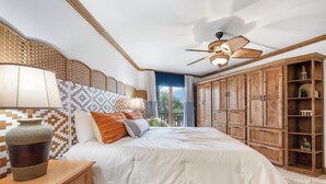 Un dormitorio con una cama grande, cabecera de madera, ventilador de techo y vistas al exterior.