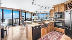 Una cocina con una isla grande, electrodomésticos de acero inoxidable, armarios de madera y vistas al océano.