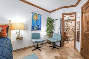 A room with a bed, two chairs, a lamp, a painting, a plant, and a bathroom visible through an open door. - Sea Gull #304: Beachfront 2 Bedroom 2 Bathroom With Spectacular Views and 24 Hour Management (Port Aransas)