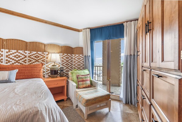 Ein Hotelzimmer mit Bett, Stuhl, Nachttisch, Lampe und Blick ins Freie durch eine Schiebetür.