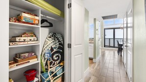 Een gang met een witte deur die uitkomt op een balkon. Aan de linkerkant staan planken met verschillende gezelschapsspellen en een surfboard.