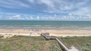 A beach with a wooden boardwalk leading to the shore, a sandy beach, and a few umbrellas. - Sea Gull #704: Beachfront 2 Bedroom 2 Bathroom With Spectacular Views and 24 Hour Management (Port Aransas)