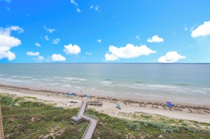 A beach with a wooden boardwalk leading to the shore, clear blue sky, and calm sea.