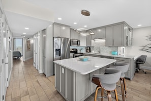 A modern kitchen with a central island, stainless steel appliances, and a herringbone-patterned backsplash.