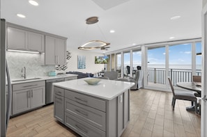 A modern kitchen with grey cabinetry, a central island, and a dining area with a view.