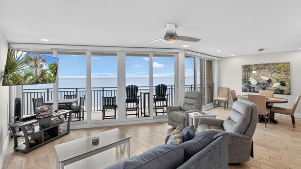 A spacious living area with a balcony, large windows, a ceiling fan, and a flat-screen TV. - Sea Gull #906: Beachfront 2 Bedroom 2 Bathroom With Spectacular Views and 24 Hour Management (Port Aransas)