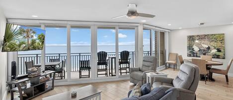 A spacious living area with a balcony, large windows, a ceiling fan, and a flat-screen TV.