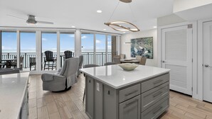 A spacious kitchen with a large island, a dining area with chairs, and a view of the ocean. - Sea Gull #906: Beachfront 2 Bedroom 2 Bathroom With Spectacular Views and 24 Hour Management (Port Aransas)