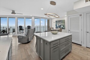 A spacious kitchen with a large island, a dining area with chairs, and a view of the ocean.