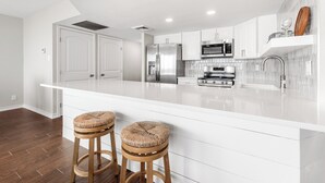 A modern kitchen with white cabinetry, stainless steel appliances, and a large island with stools. - Sea Gull #609: Beachfront 2 Bedroom 2 Bathroom With Spectacular Views and 24 Hour Management (Port Aransas)