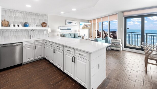 A modern kitchen with white cabinetry, a large island, and a view of the ocean through the sliding glass doors. - Sea Gull #609: Beachfront 2 Bedroom 2 Bathroom With Spectacular Views and 24 Hour Management (Port Aransas)
