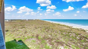 Un paisaje costero con playa, terreno cubierto de hierba y cielo azul despejado.
