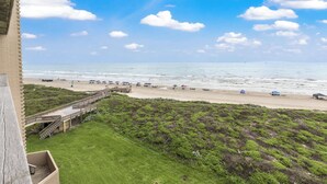 A beach view from a balcony with a wooden deck, grassy area, and beach amenities like umbrellas and beach chairs. - Sea Gull #509: Beachfront 2 Bedroom 2 Bathroom With Spectacular Views and 24 Hour Management (Port Aransas)