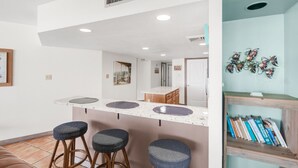 A kitchen with three bar stools, a countertop with three sinks, and a wooden cabinet.