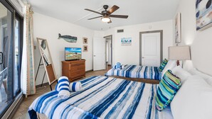 A hotel room with two beds, a ceiling fan, a dresser, and artwork on the walls.