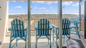 A balcony with blue Adirondack chairs and a table, overlooking a beach and ocean.
