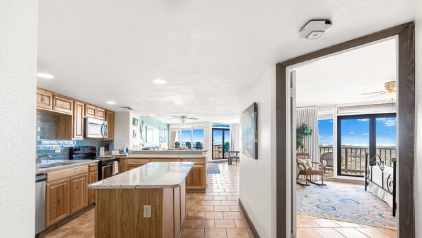 A spacious kitchen with wooden cabinets, a central island, and a view to a balcony.