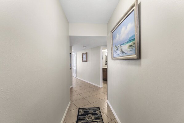 A hallway with a tiled floor, a rug, and a framed painting on the wall.