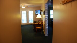 Un salon avec un ventilateur de plafond, un téléviseur, une lampe et un fauteuil.
