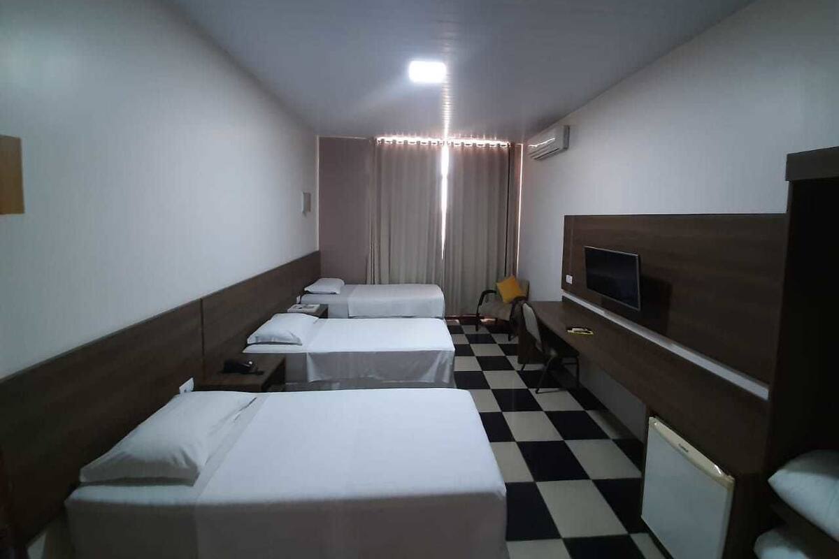 A hotel room with three single beds, a TV, a small desk, and a checkered floor.