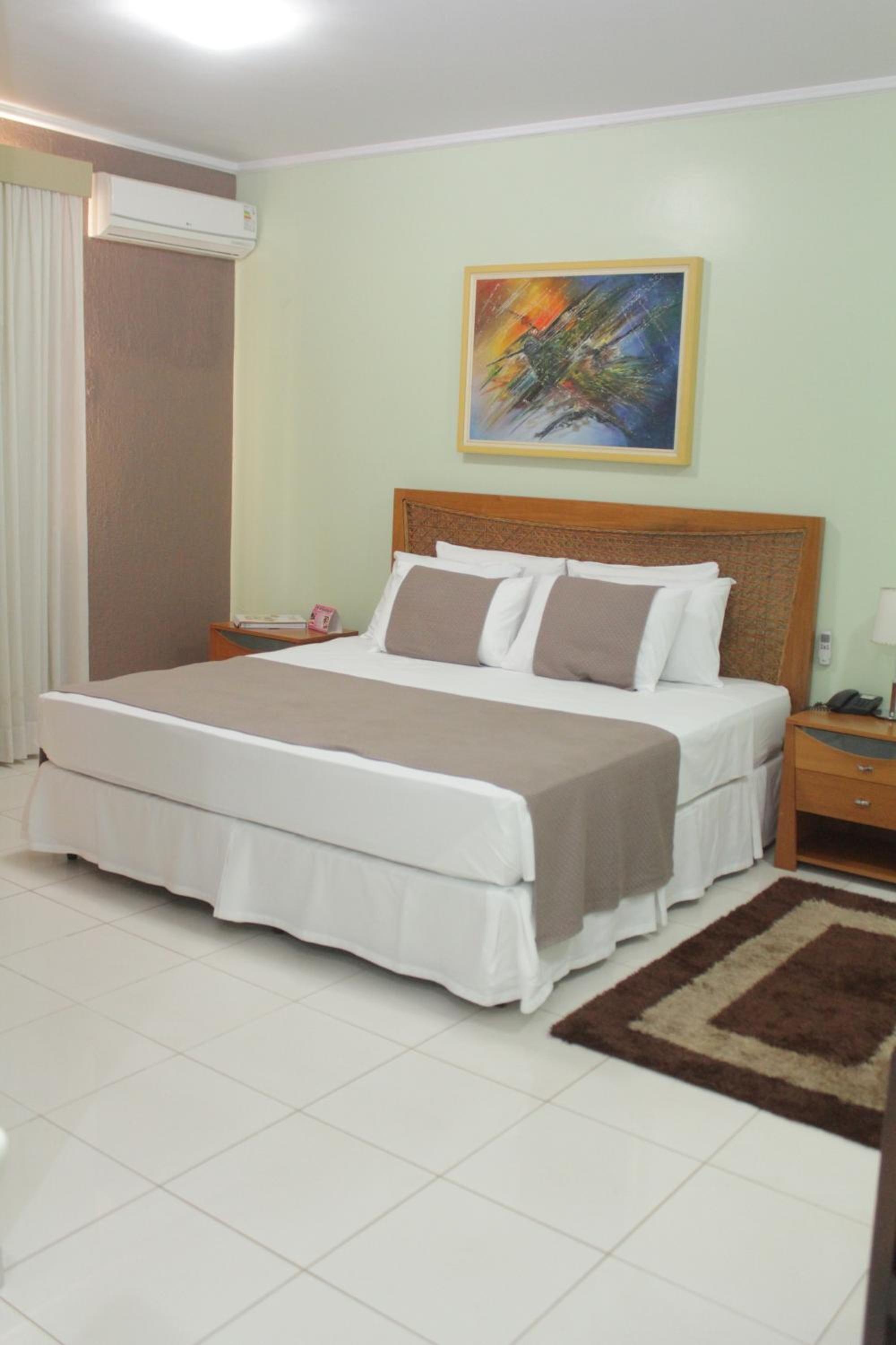 A neatly arranged bedroom with a large bed, a bedside table with a lamp, and a wall-mounted air conditioner.