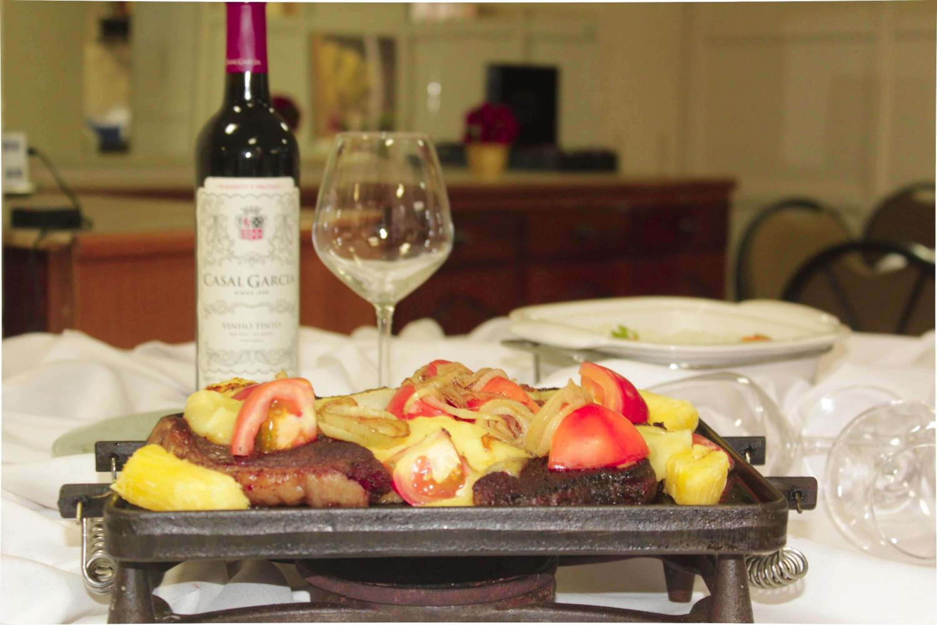 A steak with vegetables on a grill, a bottle of wine, and a wine glass on a table.