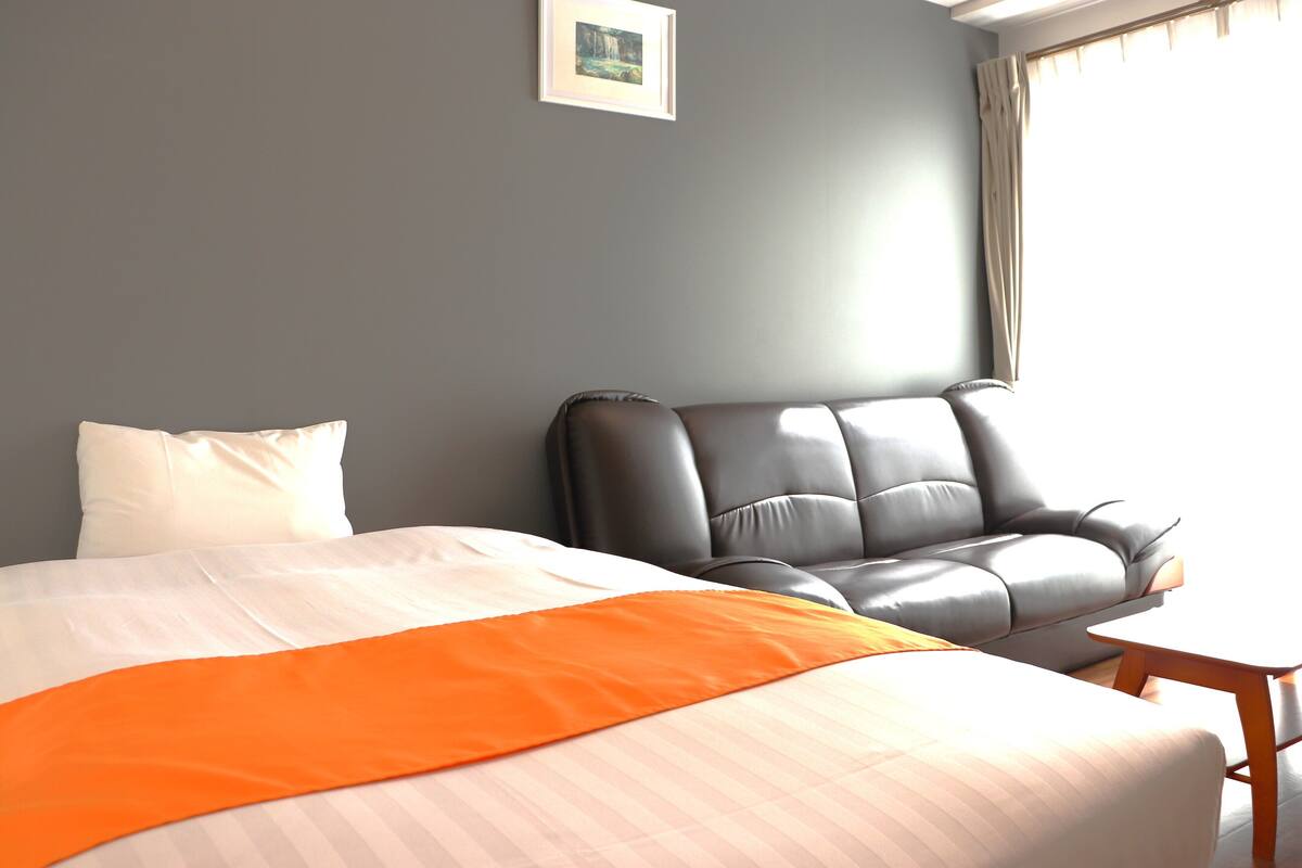 A hotel room with a bed, a grey sofa, and a small wooden table.