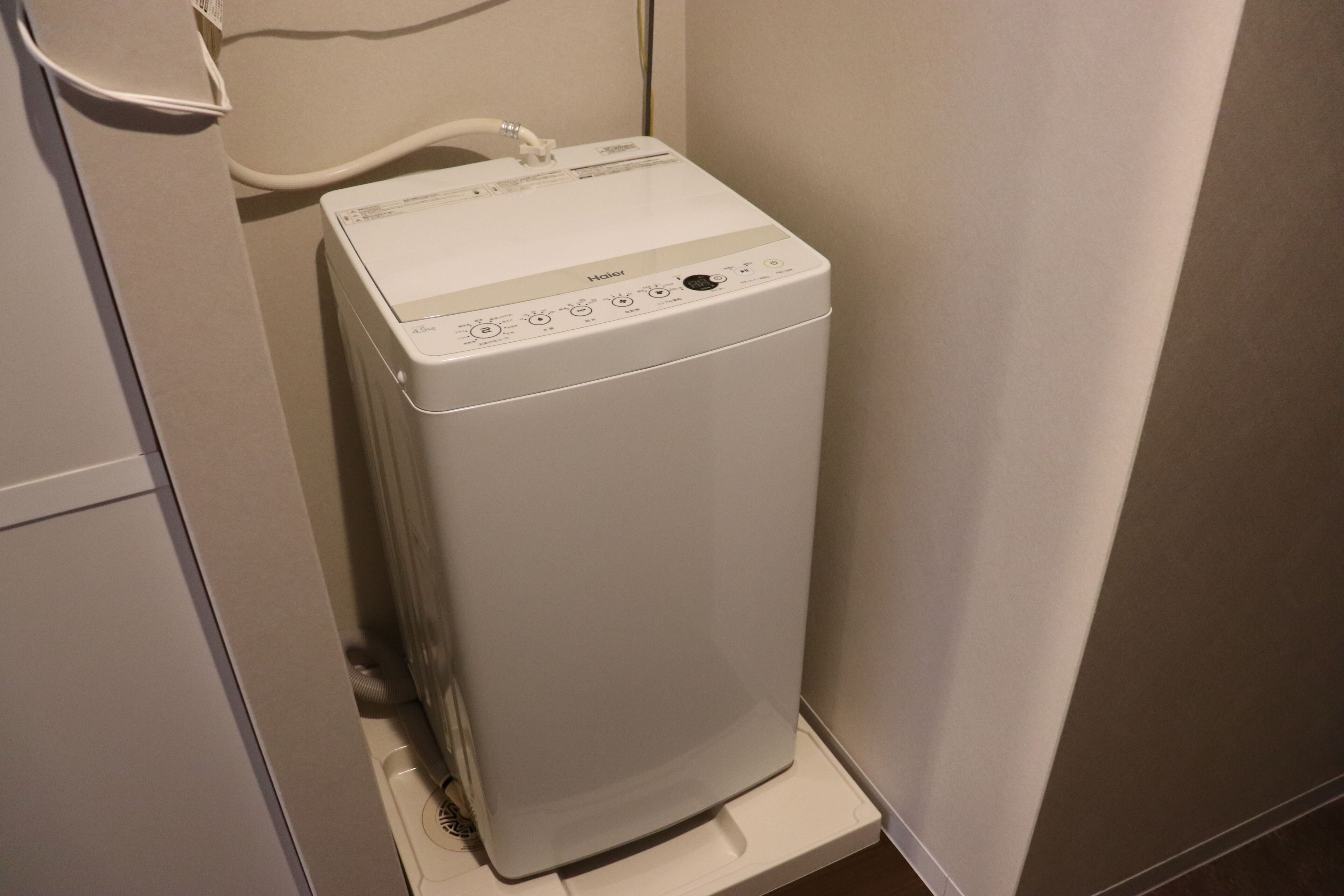 Een compact wit was- en droogcombinatie in een kleine wasruimte met een witte muur en een houten vloer.