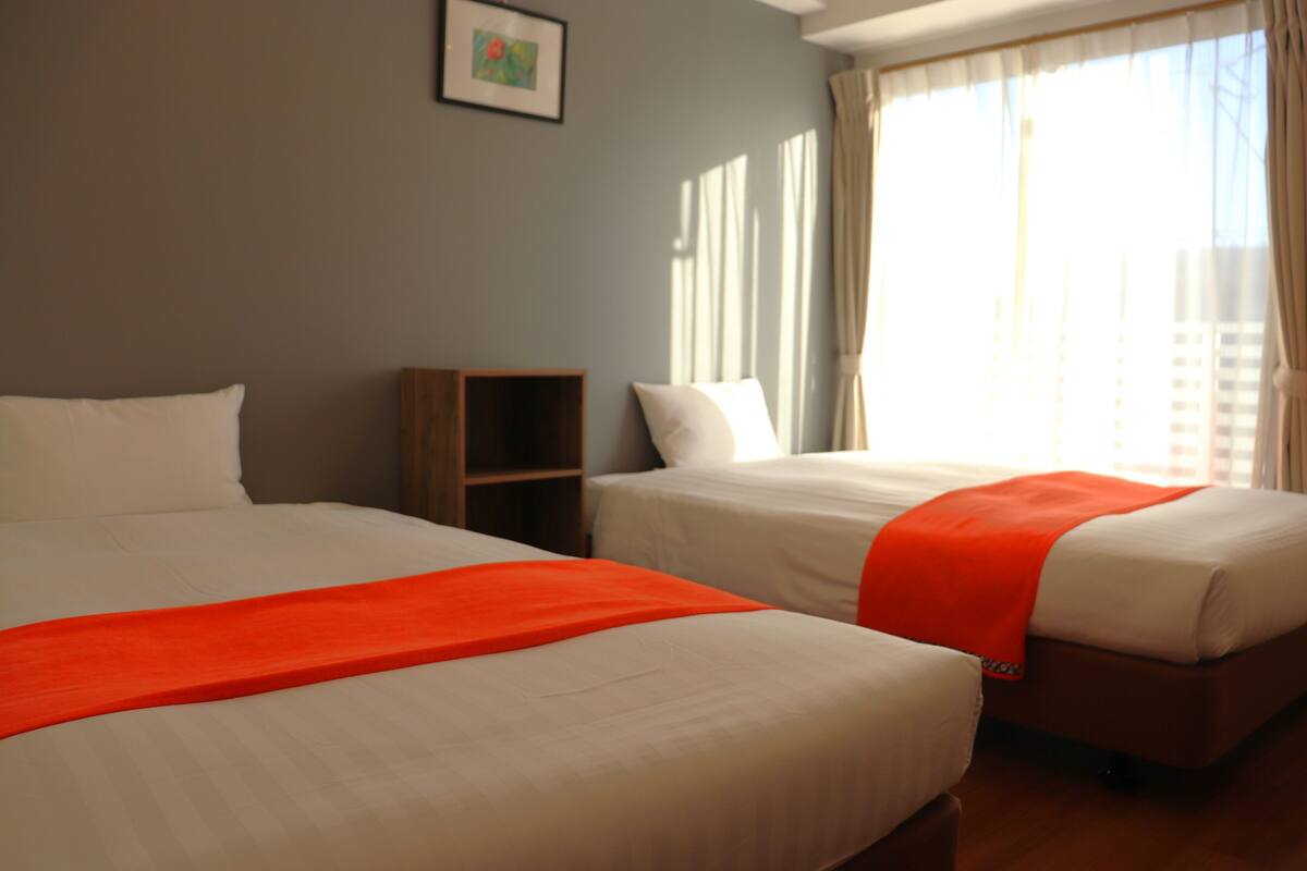A hotel room with two beds, a small wooden cabinet, and a window with curtains.