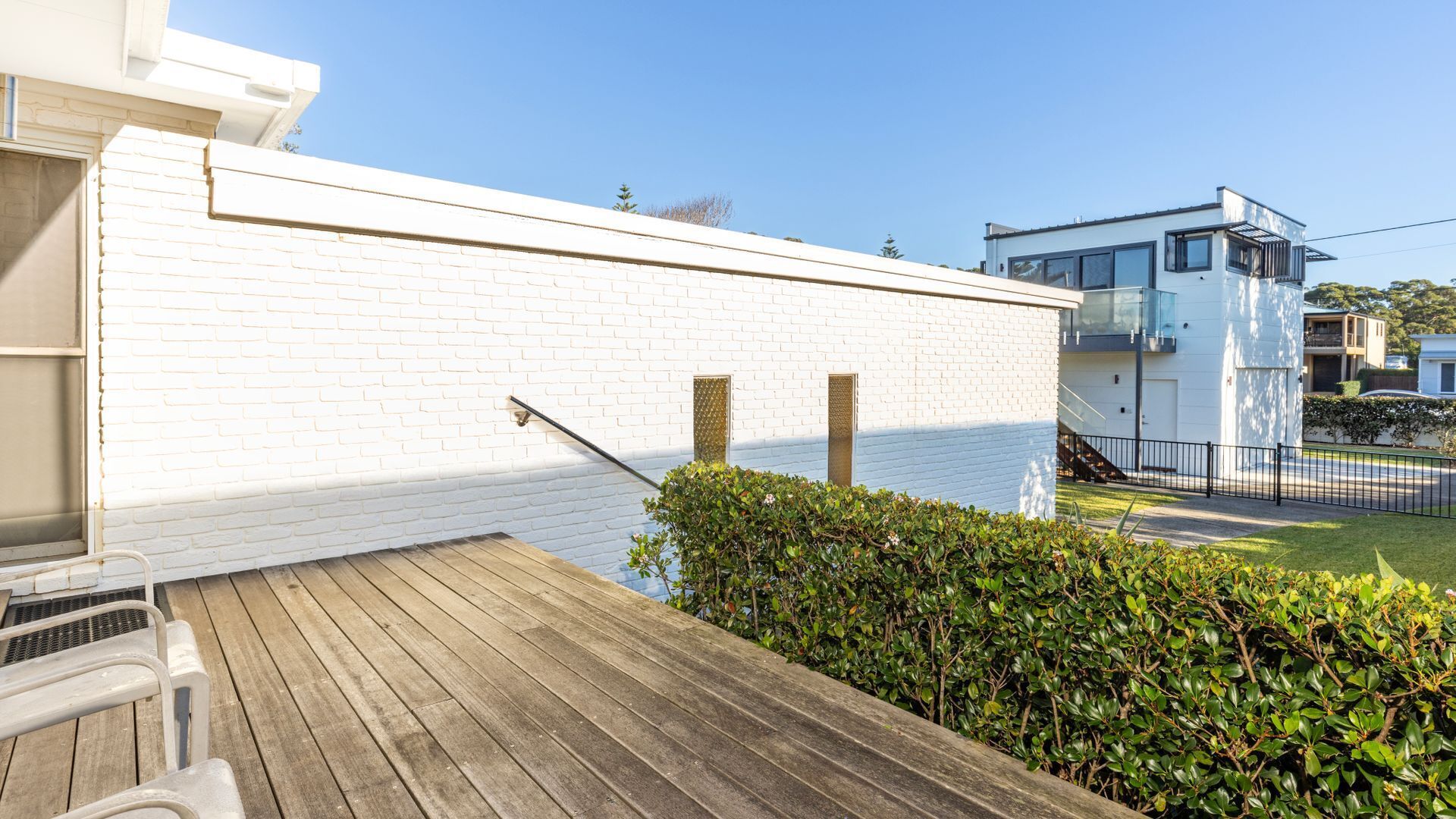 A white brick building with a wooden deck and a metal railing.