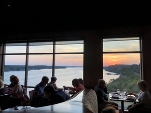 Un restaurant doté de grandes fenêtres offrant une vue sur une rivière et le coucher du soleil.
