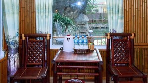 A room with two wooden chairs, a table, a kettle, and a basket with bottles. - Trang An Mountain House - Bungalow Deluxe with garden view - Ninh Binh (Ninh Binh)