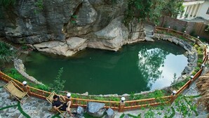 A circular stone pool with a wooden fence, surrounded by greenery and a stone pathway. - Trang An Mountain House - Bungalow Deluxe with garden view - Ninh Binh (Ninh Binh)