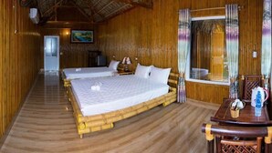 A room with a large bed, a smaller bed, a wooden table, and a window with curtains. - Trang An Mountain House - Bungalow Deluxe with garden view - Ninh Binh (Ninh Binh)