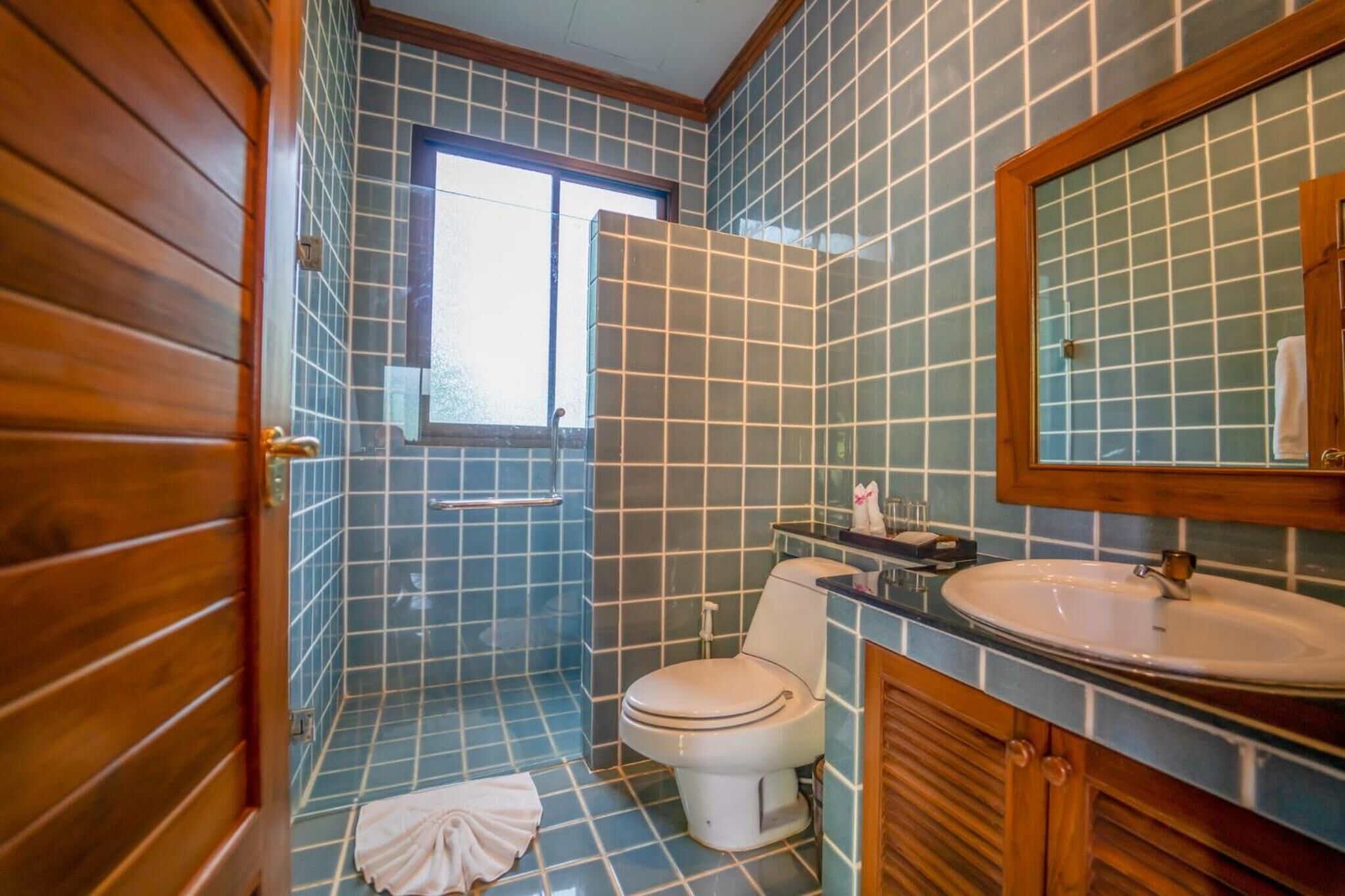 Un baño con paredes de azulejos azules, una puerta de madera, un inodoro blanco, un lavamanos y un espejo.