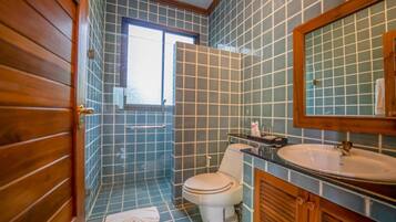 Un baño con paredes de azulejos azules, una puerta de madera, un inodoro blanco, un lavamanos y un espejo.