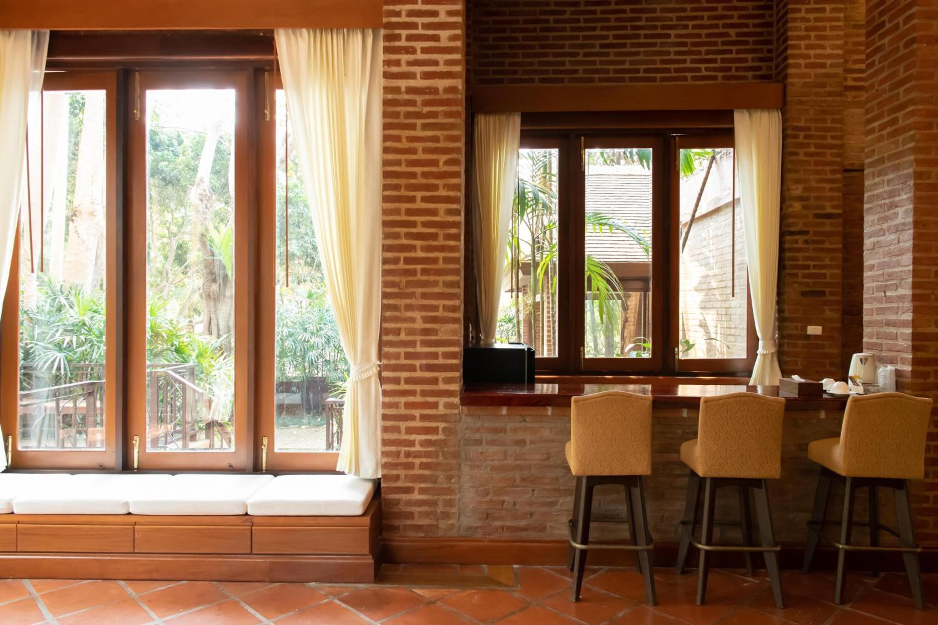 Una habitación con pared de ladrillo, ventana con cortinas, un banco y tres taburetes.