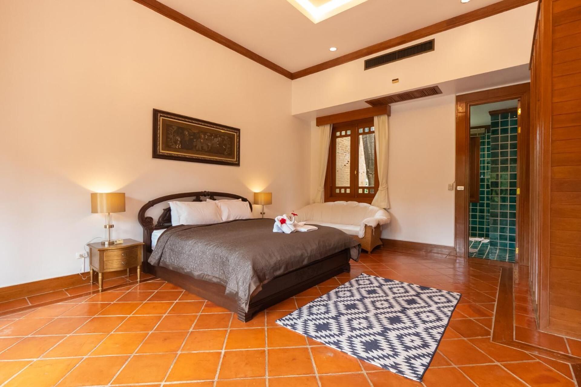 A bedroom with a bed, two bedside tables, a nightstand, a patterned rug, and a door leading to a bathroom.