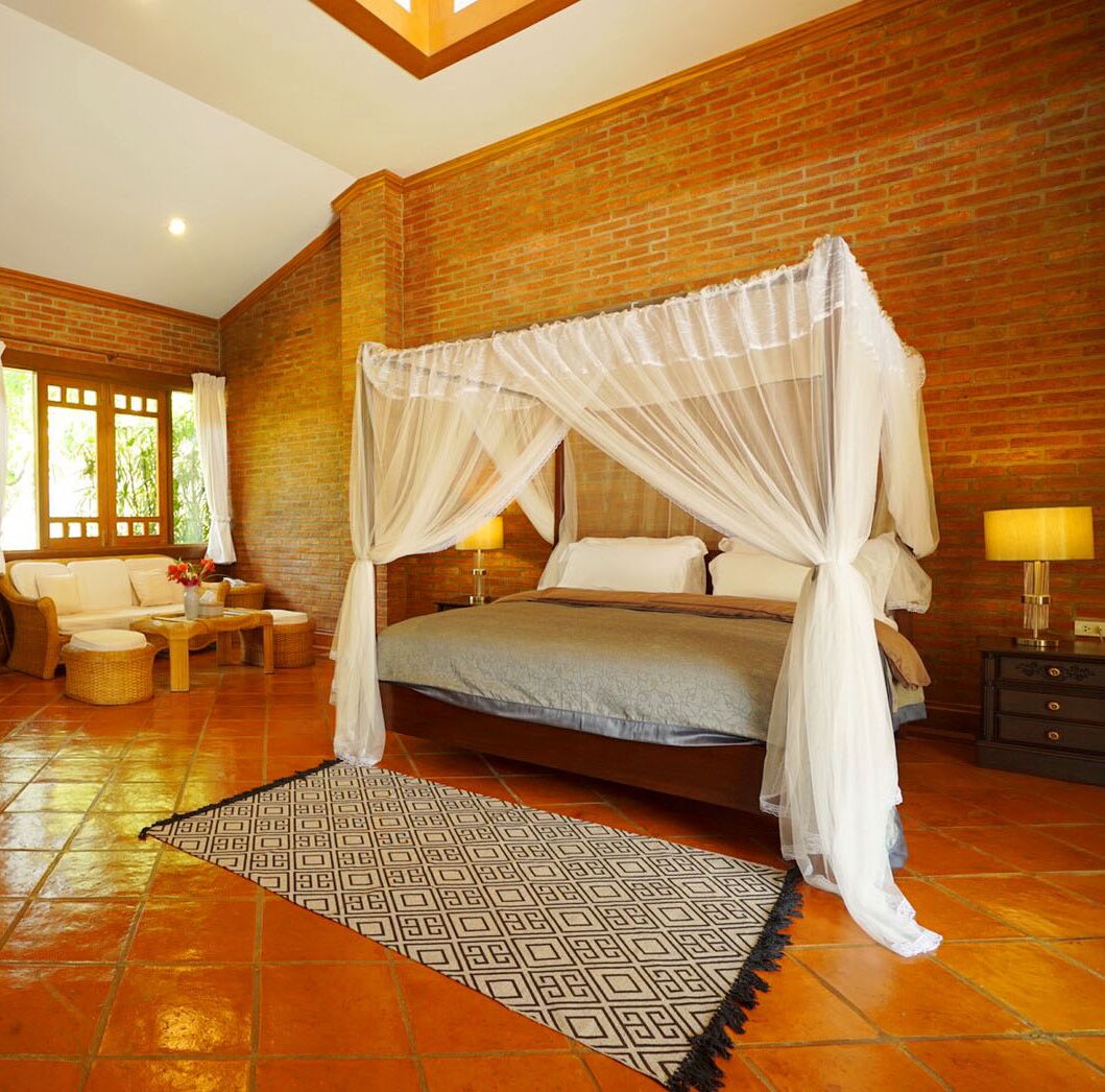 A spacious bedroom with a four-poster bed, a sitting area with a sofa and chairs, and a large window providing natural light.