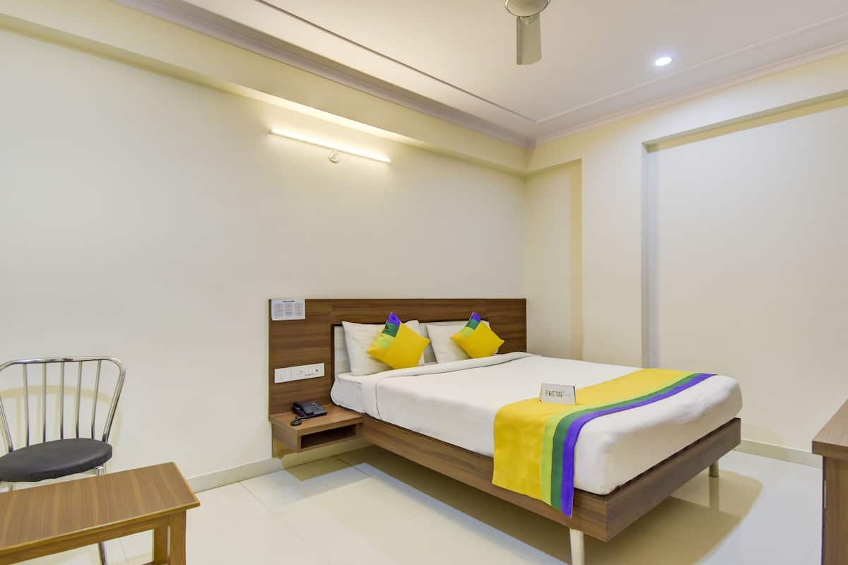 A hotel room with a wooden bed, a bedside table with a phone, a chair, and a small desk.
