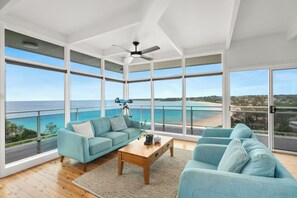 A spacious living room with a large view of the ocean, a ceiling fan, and a wooden coffee table. - Outstanding ocean views (Mollymook Beach)