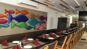 A restaurant with a long dining area, multiple tables set with red napkins, and a wall decorated with colorful fish sculptures. - Hotel Bindra Supremacy (Mumbai)