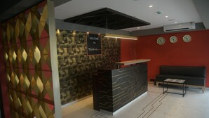 A reception area with a modern design, including a patterned wall, a welcome sign, and a seating area with a sofa and a small table. - Hotel Bindra Supremacy (Mumbai)