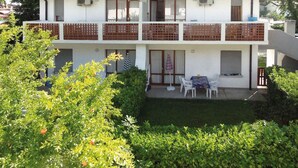 Ein zweistöckiges Gebäude mit Balkon, kleinem Garten und Tisch mit Stühlen.