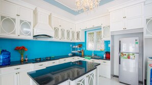 A kitchen with white cabinets, a black countertop, a stainless steel refrigerator, and a blue backsplash. - DREAM HOUSE VILLA Vung Tau (Tp. Vũng Tàu)