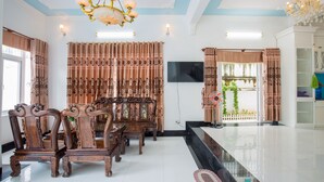 A spacious living room with a large TV, elegant wooden furniture, and a chandelier. - DREAM HOUSE VILLA Vung Tau (Tp. Vũng Tàu)