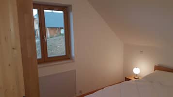 Ein Schlafzimmer mit einem Einzelbett, einem Nachttisch mit Lampe, einem Fenster mit Blick auf ein Gebäude und eine unbefestigte Fläche vor dem Fenster.
