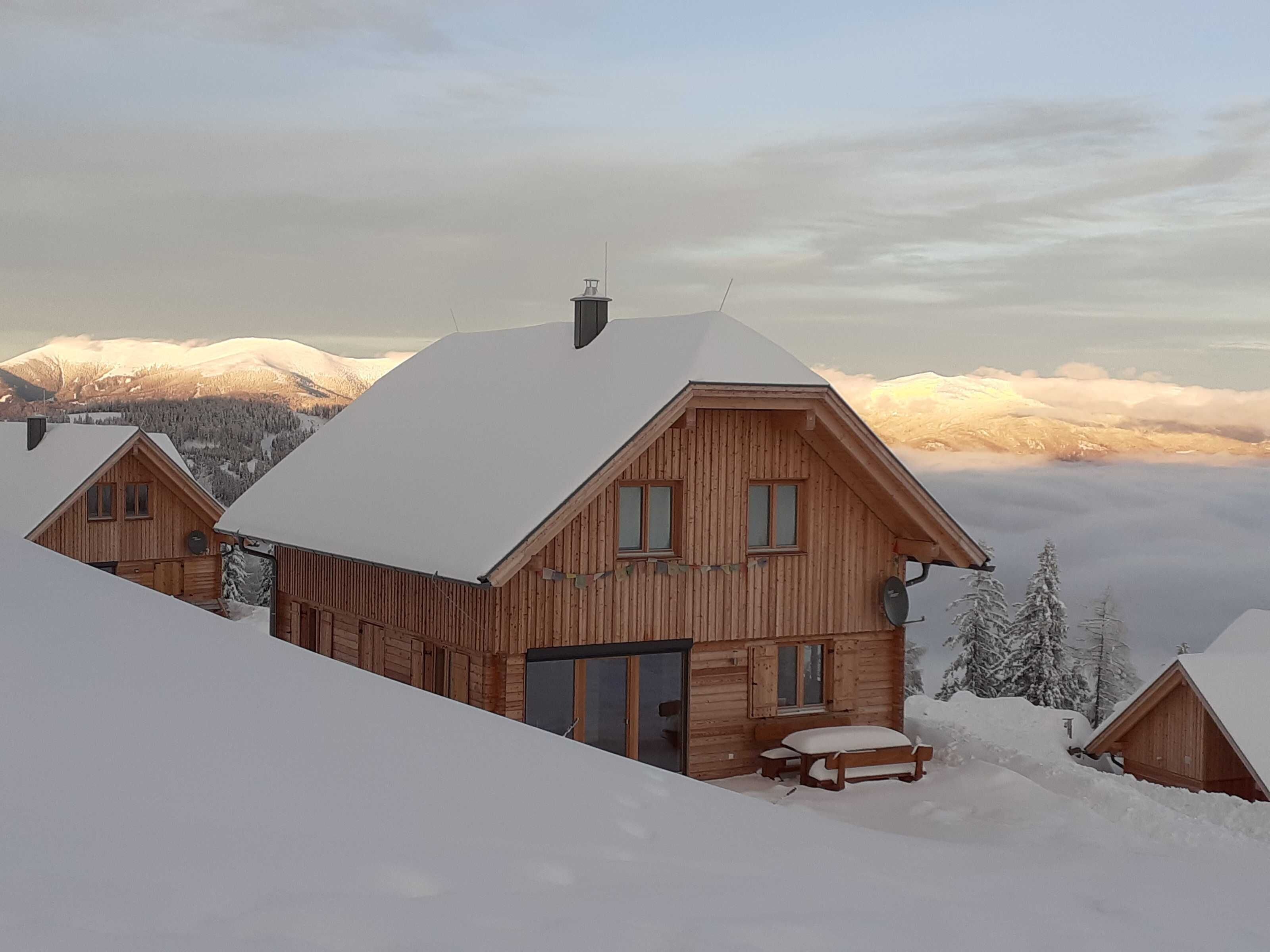 Un chalet en bois, avec un toit enneigé, un balcon et une vue sur des montagnes couvertes de neige.